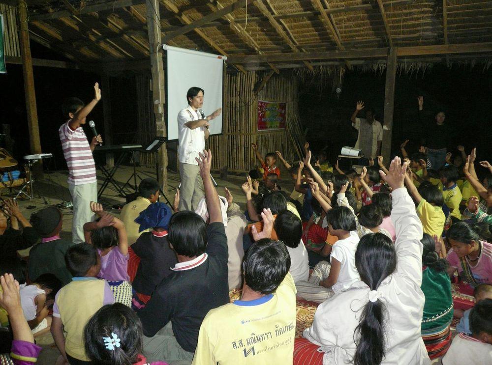 Pastor Steve Cioccolanti leading a village ministry gathering in rural Thailand with hands raised in worship
